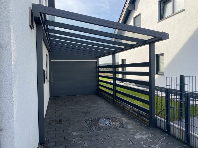 Carport mit Glasdach und Aluminiumkonstruktion in Anthrazit über einem gepflasterten Stellplatz