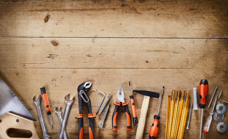Werkzeuge auf einer Holzplatte: Säge, Zangen, Hammer und Zollstock