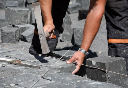 Handwerker setzt Granitpflaster mit dem Hammer entlang einer Richtschnur