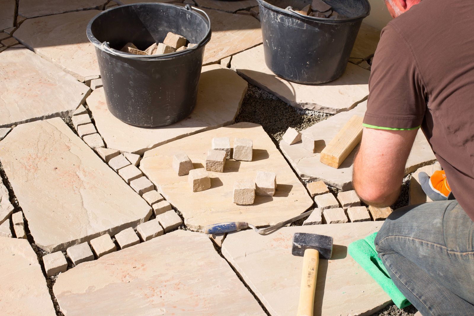 Verlegen von Natursteinplatten mit kleinen Pflastersteinen als Fugenband