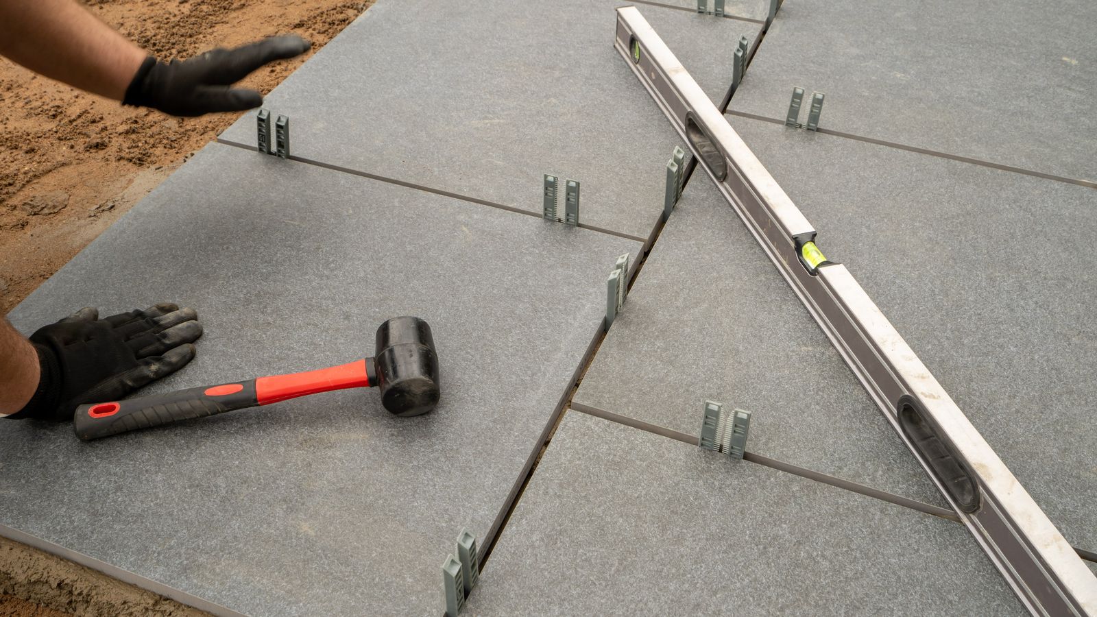 Große Terrassenplatten werden auf Sand verlegt und mit der Wasserwaage geprüft